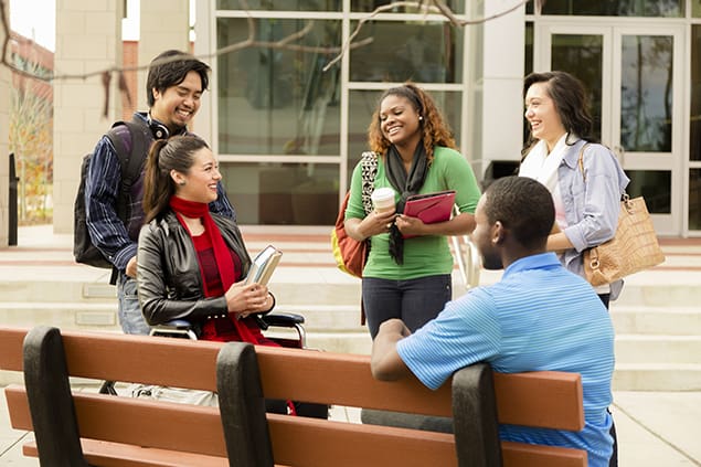 A group of college students talk outside school building.