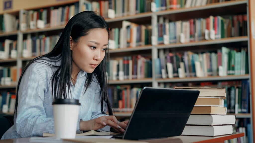 A young woman works on a laptop in a library