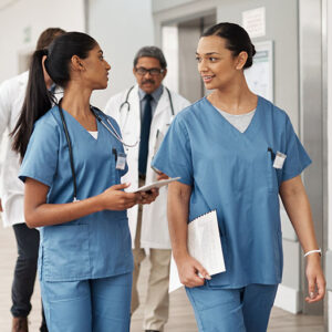 Two nurses converse with two doctors in the background