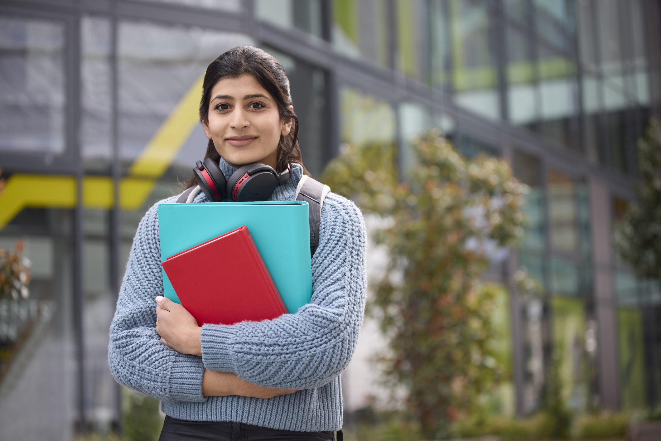 Female College Or University Student Outside Campus Building Wearing Wireless Headphones
